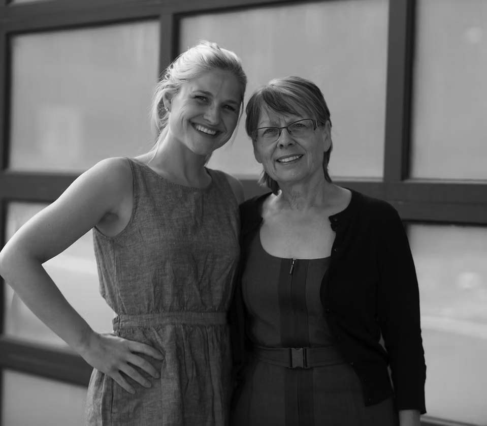 support-services-2 Two women standing close together and smiling at the camera—one younger with blonde hair in a blue sleeveless dress, the other older with short brown hair, glasses, and a dark cardigan—enjoying time outdoors by a building after receiving Pavelcomm Support.