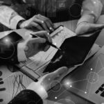 Three people collaborate at a desk with charts, a laptop, and a tablet, discussing data and analytics. Digital graphics highlight cloud computing and network connections, emphasizing teamwork and the advantages of technology in business analysis.