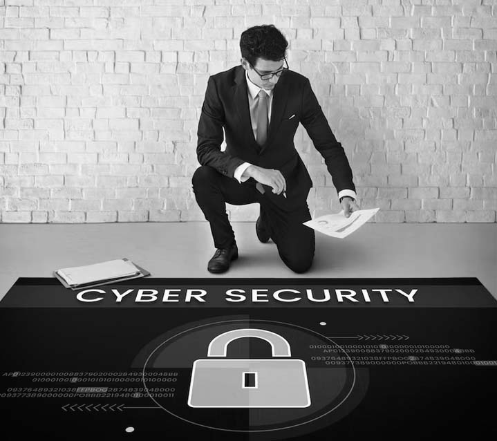A man in a suit kneels on one knee, holding papers next to a clipboard. He faces a floor graphic with CYBER SECURITY and a padlock icon, highlighting IT security awareness for Portland businesses.