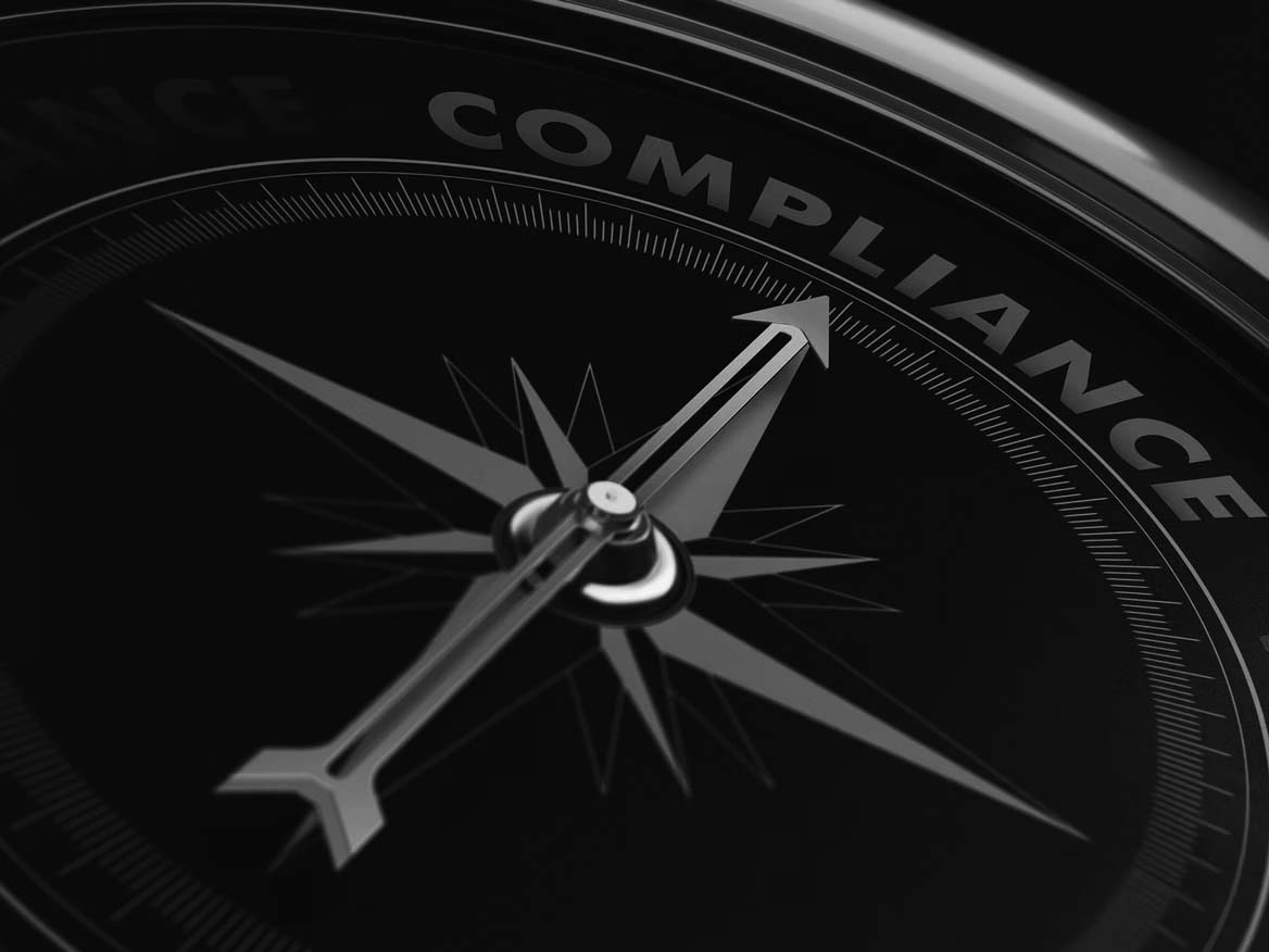 A close-up of a black compass with the needle pointing to the word COMPLIANCE—highlighted in blue and red accents—symbolizes regulatory compliance and professional compliance solutions.