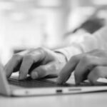 Close-up of a person's hands typing on a laptop keyboard, focused on data cleaning tasks, with a blurred background and a hint of greenery.